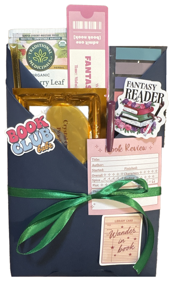 A blind date book wrapped in navy paper and tied with a green ribbon, tucked with tea, a bookmark, sticky tabs, stickers, a book review card and a library card